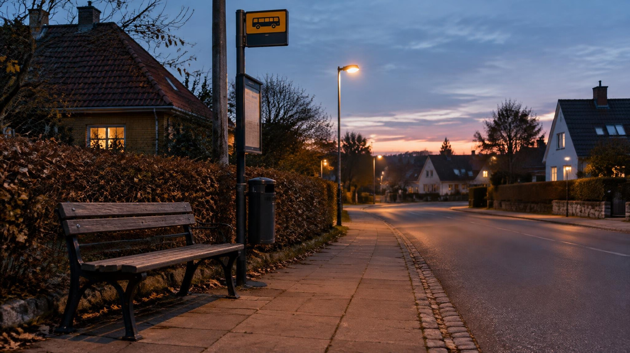 Empty park bench and bus stop sign on a quiet Danish street in the evening